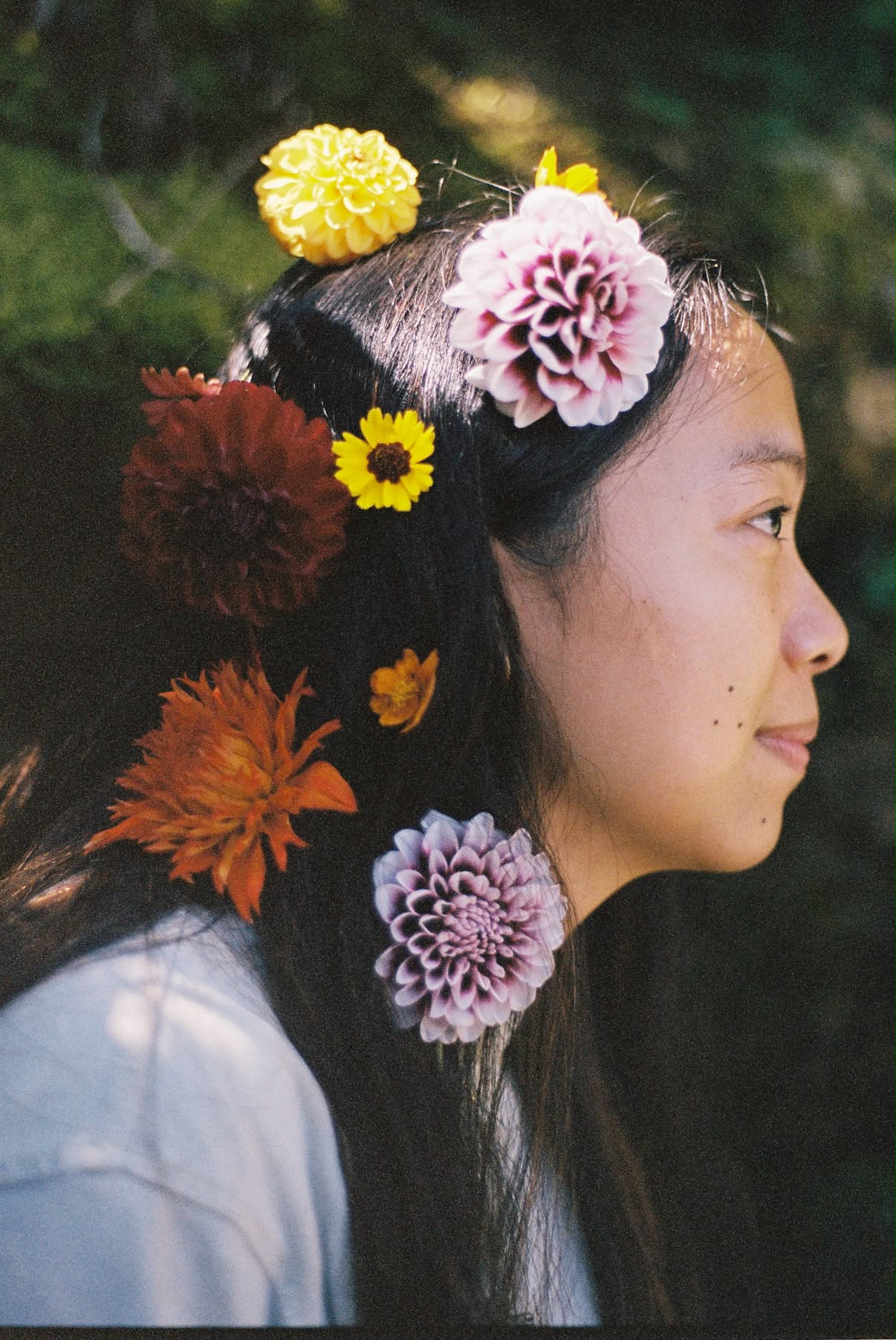 Film photograph in profile of a dark-haired woman with dahlias and wildflowers tucked through her hair