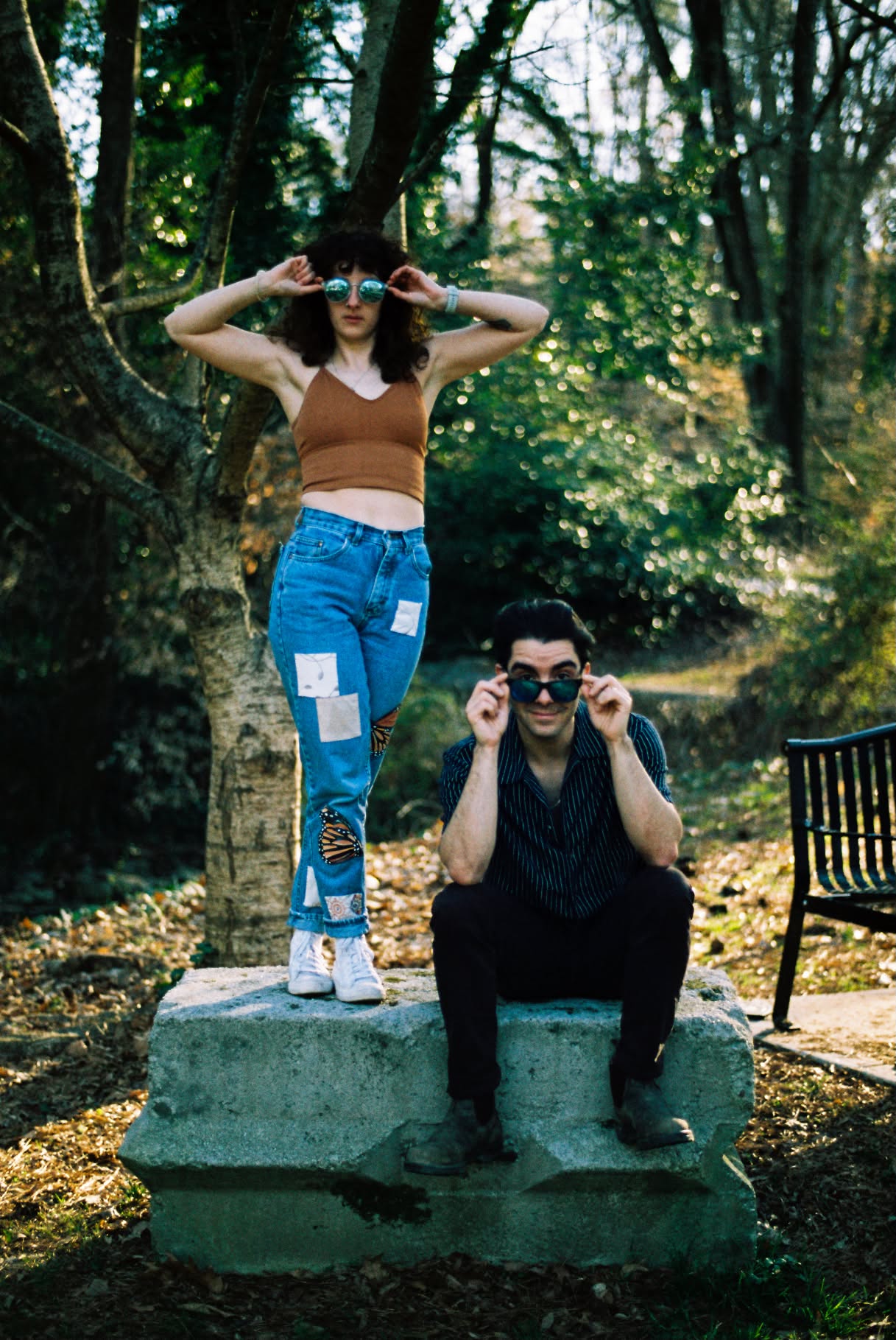 Film photograph of two people lowering their sunglasses while posing on a concrete block in the woods