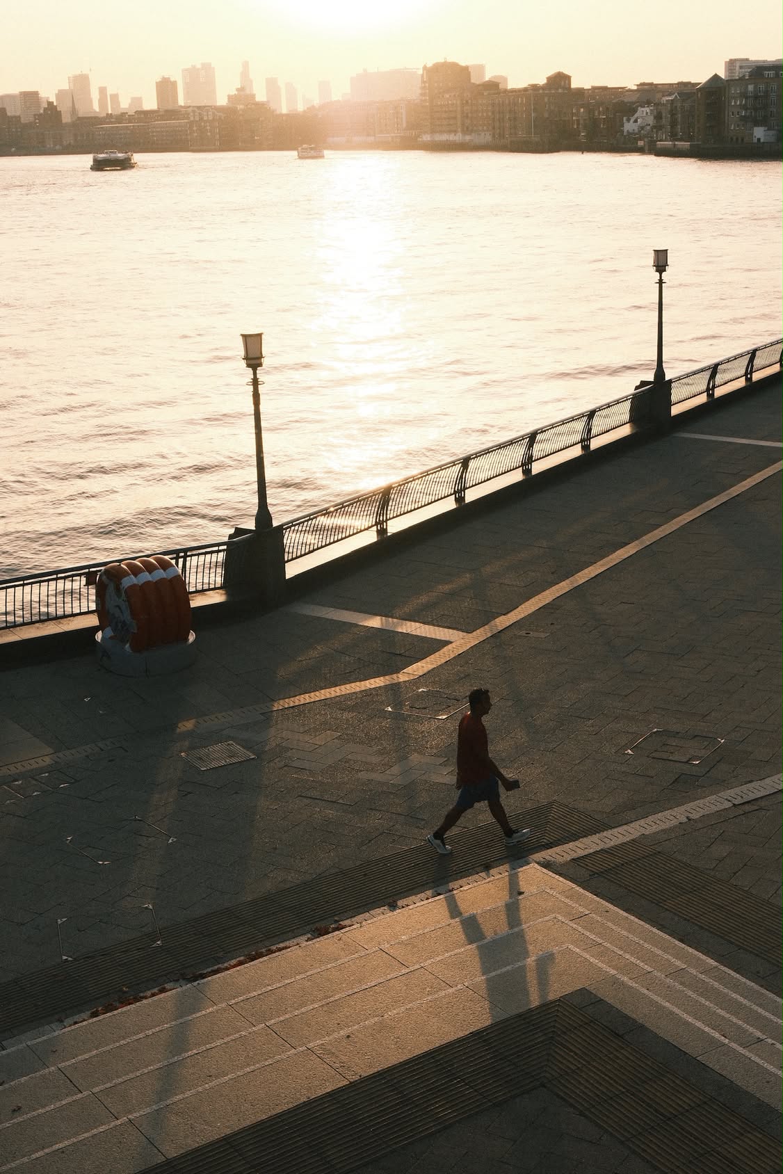 Photograph of a lone figure walking along the Thames at golden hour, warm light spilling across the water