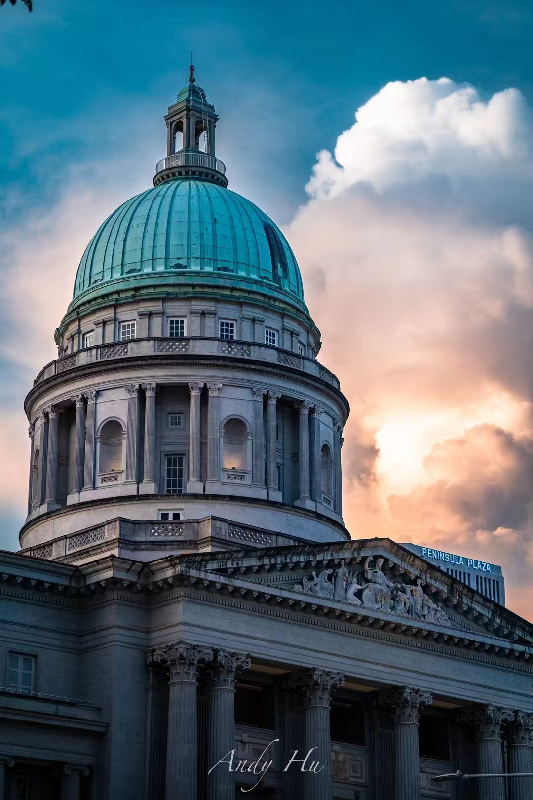 Photograph of a colonial-era teal-domed building with classical columns against dramatic storm clouds lit by sunset